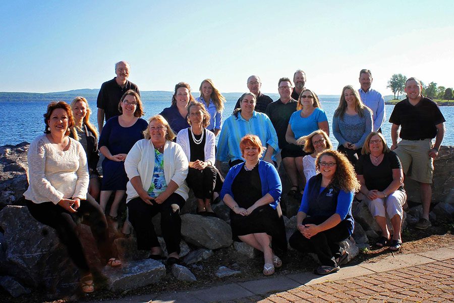 About Our Agency - Portrait of the Harbor Brenn Insurance Agencies Team Sitting on Rocks By the Coast on a Sunny Day in Petoskey Michigan