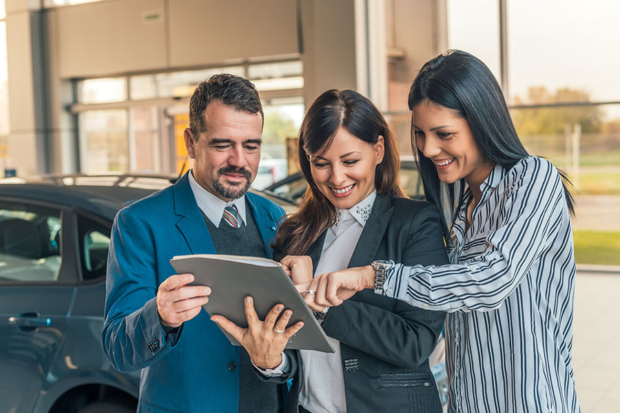 Auto Change Information Form - Portrait of a Smiling Car Dealership Sales Agent Showing Her Two Clients the Contract for Their New Car Purchase